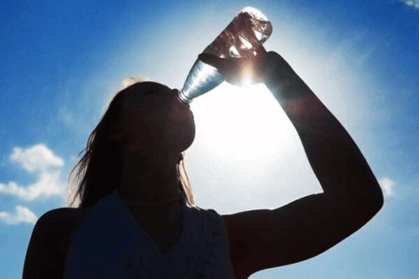 A woman drinking water from a bottle in the sun.