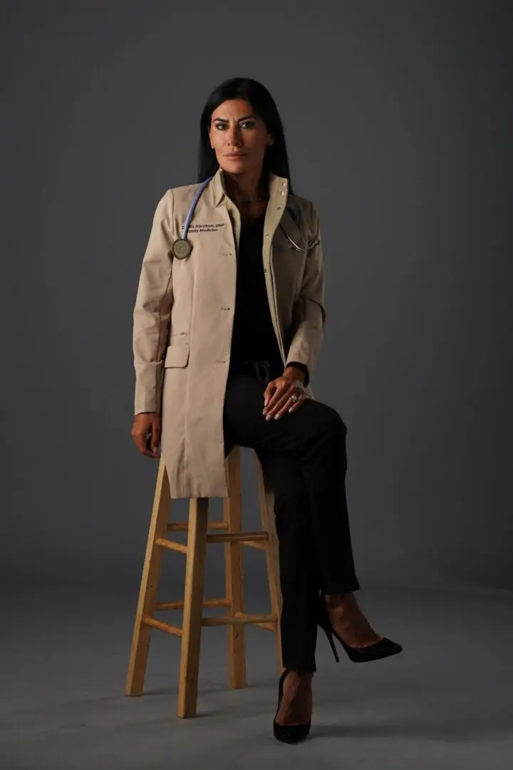 A woman sitting on top of a stool wearing a lab coat.